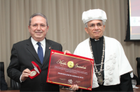 Foto do desembargador Carvalho Neto, de terno escuro e seguranda a medalha e o diploma entregues pelo reitor da Natalino Salgado, à sua esquerda.