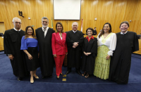 Foto posada de quatro mulheres e quatro homens à frente de parede de ripas amadeiradas e sobre carpete azul escuro.