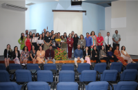 Foto de diversas pessoas (mulheres e homens) sentados e em pé no palco do auditório Juiz Ari Rocha