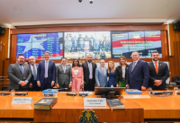 mesa de plenário com 11 pessoas reunidas para a foto. Ao fundo, painel com imagens da bandeira do maranhão 