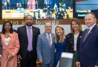 três homens e três mulheres posam para foto em solenidade. Ao fundo, painel com imagens do evento