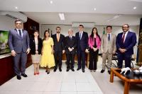 três mulheres e seis homens posam para a foto. Compõem a imagem uma mesa de centro e uma televisão na lateral esquerda. 