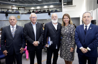 Foto de três desembargadores, uma desembargadora e palestrante. Todos estão lado a lado e em posicionados  no palco do auditório.