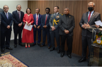 Sete homens usando ternos escuros, sendo um militar, e uma mulher de vestido que estão em pé e lado a lado.