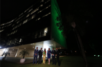 Foto de quatro homens e duas mulheres à frente da fachada do prédio do TST, iluminada de verde.