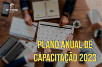 Foto de um calendário sobre uma mesa. Em volta dele, mãos de dois homens e uma mulher em atividade de análise das datas. No canto inferior direito, o texto PLANO ANUAL DE CAPACITAÇÃO 2023 em amarelo.