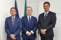 Fundo de parede na cor branca. À frente, 3 homens de terno no tom escuro posam para a foto