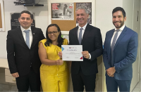 Quatro pessoas em pé posando para foto. As duas pessoas que estão na posição central seguram um certificado. Ao fundo, mural com papel fixado escrito "TODOS JUNTOS CONTRA O TRABALHO INFANTIL".