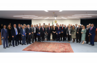 Grupo de pessoas reunidas posando para foto, em um auditório. Ao fundo, brasão da República do Brasil.