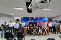 Grupo de pessoas posando para foto em sala de auditrório. No centro, quatro mulheres sentadas em cadeiras e outras pessoas, dos extremos, em pé. Ao fundo, parede azul. 