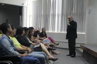 Homem com microfone na mão em um auditório ministrando palestra para alunos.