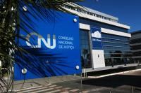 Fachada de edifício da sede do Conselho Nacional de Justiça. No primeiro plano, painel com o nome do CNJ.