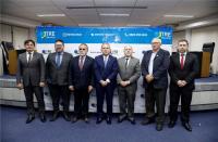 Homens posando para foto, vestidos com ternos, em uma sala de auditório.