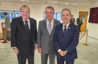 Três homens posando para foto, ambos vestidos com ternos. O homem da esquerda veste terno preto, o do meio veste terno cinza claro e o da direita veste terno azul. 