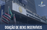 Fachada do prédio-sede do TRT16 com bandeiras hasteadas do Brasil, do Maranhão e do Tribunal. Abaixo, texto Doação de Bens Inservíveis na cor branca. No canto superior à direita, logomarca do Tribunal na cor branca.