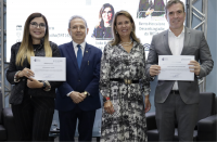 Foto de duas mulheres e dois homens em pé. Estão num auditório e uma das mulheres e um dos homens seguram um certificado.