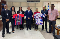 Foto de três mulheres e quatro homens em pé em uma sala. Duas mulheres seguram uma camisa com listras verticais e uma parte lisa, nas cores vermelha, azul, branca e preta; e um homem e outra mulher seguram uma camisa com fundo branco e figuras nas cores azul, vermelha e preta.