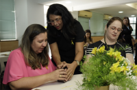 Foto de três mulheres preparando ikebanas com um arranjo de flores amarelas em primeiro plano.