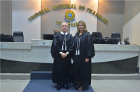 Um homem e uma mulher posam para foto dentro de um plenário. Ambos vestindo toga.