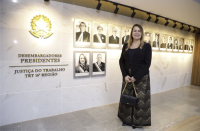 Mulher posando para foto em frente a galeria de desembargadores presidentes do TRT-16. 