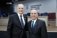 Dois homens usando terno preto posam para foto dentro de um auditório.