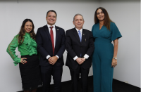 Quatro pessoas posando para foto. Dois homens no centro e duas mulheres. Os homens estão de usando terno e calça social na cor preta e gravatas.