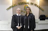 Um homem e uma mulher posam para foto dentro de um plenário. Ambos vestindo toga.