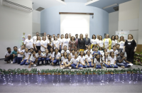 Grupo de pessoas posando para foto, dentro de um auditório. Algumas estão em pé e outras sentadas.