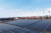   Foto de várias placas solares fotovoltaicas que estão localizadas no topo de um edifício. No segundo plano, há casas e edifícios que estão localizados mais distantes.