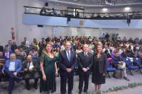 Foto de duas mulheres e dois homens de pé, à frente de uma plateia em auditório. Os quatro estão de costas para a plateia, posando para a foto.