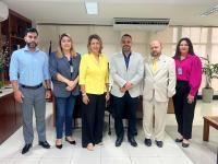 Seis pessoas posando para foto em pé, lado a lado, sendo três mulheres e três homens, dentro de uma sala com paredes brancas.