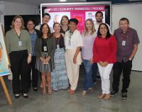 Grupo de onze pessoas posando para foto dentro de um auditório. Ao fundo, painel de led apresentando arte escrita INFECÇÕES SEXUALMENTE TRANSMISSÍVEIS E PREVENÇÃO.