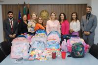 Grupo de oito pessoas posando para foto, atrás de uma mesa repleta de mochilas, com o brasão da República ao fundo.