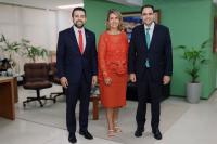 Três pessoas posando para foto dentro de uma sala. 