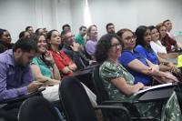 Foto de grupo de pessoas em plateia, assistindo à palestra. Ao fundo, parede branca.