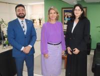 Três pessoas posando para foto dentro de uma sala. Um homem e duas mulheres.