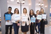 Seis pessoas posando para a foto, sendo um homem e cinco mulheres, todos estão segurando placas que se referem à inovação pública.