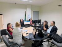 Seis pessoas reunidas em uma sala, envolta de uma mesa, em uma audiência de ocnciliação.