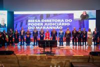 Foto tirada de uma sessão soolene de posse dentro de um auditório. Ao fundo, mesa de honra.