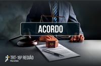 Foto de um homem usando terno, sentado, apoiando as mãos sob uma mesa. Sob a mesa itens como papel, caneta, balança da Justiça e malhete de madeira.