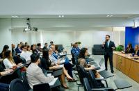 Foto de um auditório repleto de pessoas sentadas. À frente, homem palestrando.