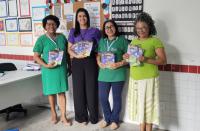 Quatro mulheres posando para foto dentro de uma sala de aula. Todas estão segurando uma cartilha em suas mãos.
