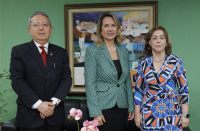 Foto de um homem e duas mulheres claros, posando para a câmera, à frente de uma parede verde, onde se vê um quadro colorido.