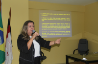 Foto com destaque para a juíza Liliana Bouéres. Ela está em pé. Atrás dela está as bandeiras no Brasil e do TRT-16
