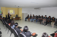 Foto mostra estudantes do EJA sentados em um auditório, ao fundo a imagem da juíza Liliana Bouéres