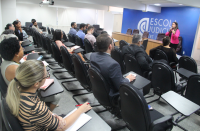 Foto mostra servidores sentados no auditório da EJUD - ao fundo a Secretária de Governança Silvia Pontes