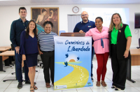 Foto mostra pessoas em pé segurando um cartaz com o nome do projeto Caminhos da Liberdade.