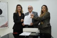 Foto com a presidente Márcia Andrea Farias, o procurador Geral do Estado Valdêncio Caminha e a juíza Joanna D´Arck. Eles seguram o edital.
