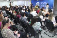 Foto mostra auditório da EJUD cheio de pessoas entre servidoras e magistradas e ao fundo em pé, a palestrante Alda Fernanda Bayma.