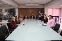 Foto mostra pessoas sentadas a mesa durante audiência de conciliação